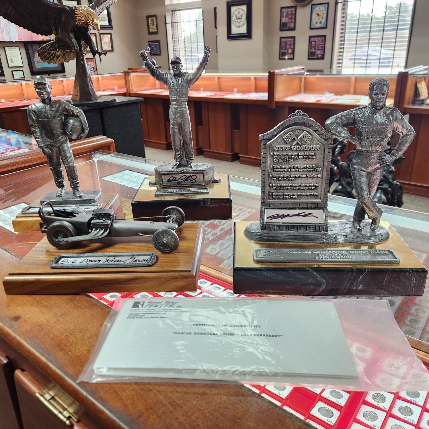 Trophy display on a wooden table with miniature racing figures and a plaque in a room with framed photos.