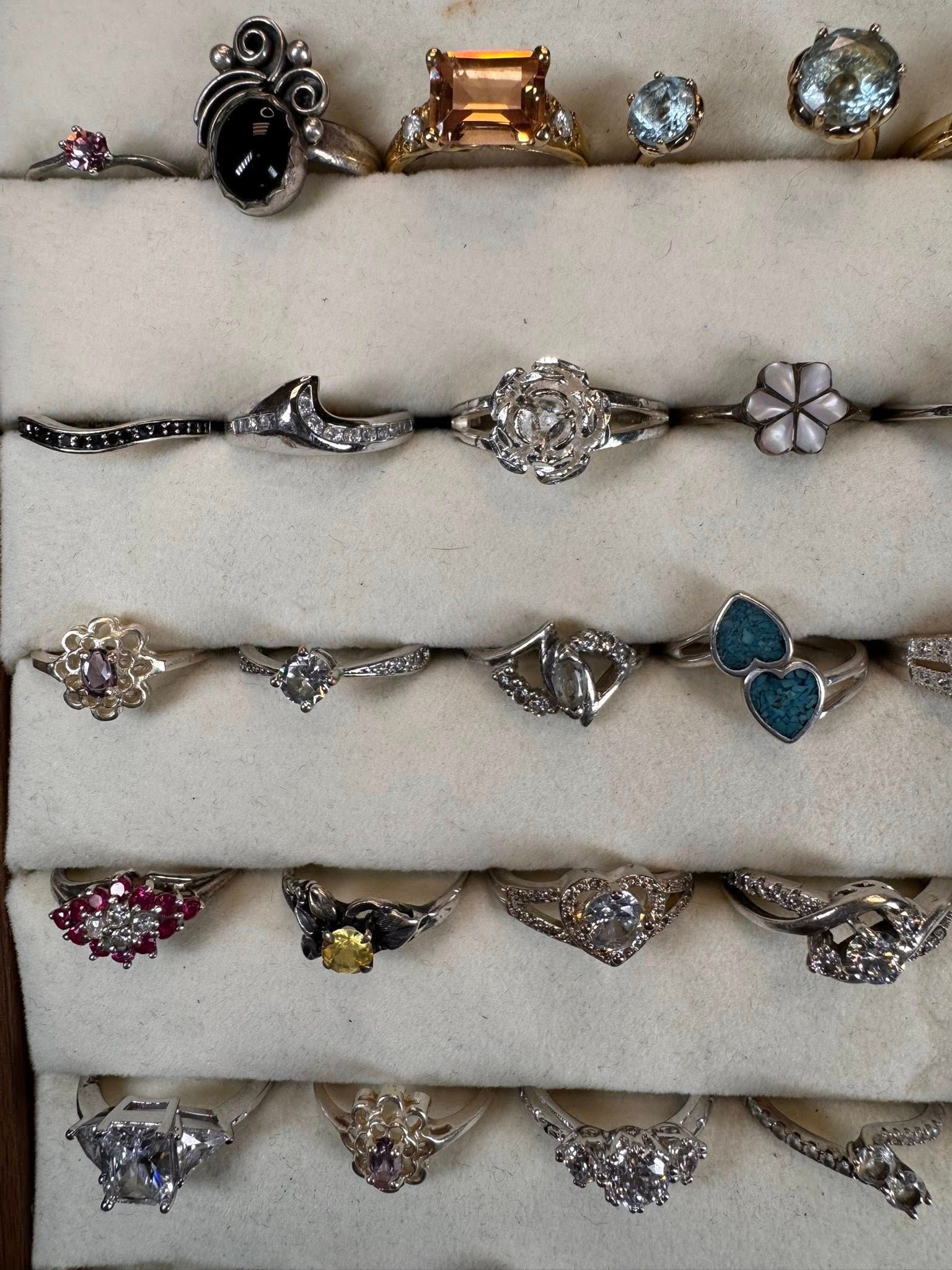 Assorted rings with gemstones and decorative settings arranged in rows on a light background
