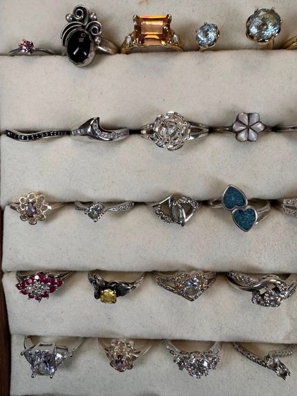 Assorted rings with gemstones and decorative settings arranged in rows on a light background