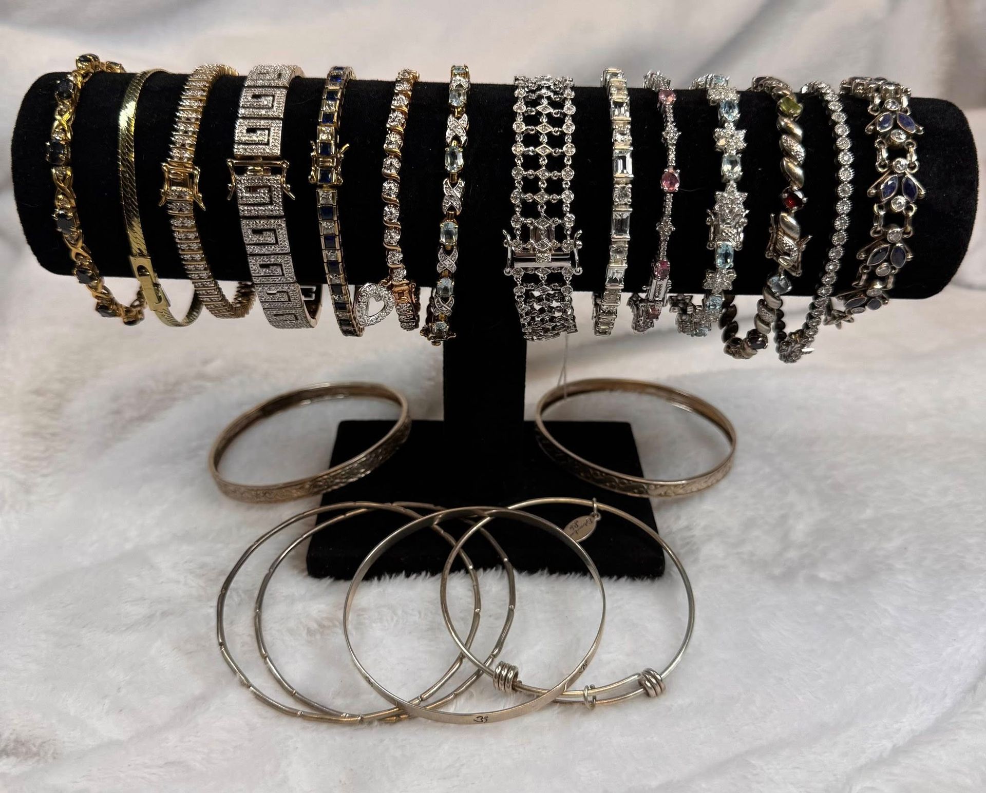 Black velvet display stand with rows of gold and silver bracelets and hoop earrings on a white fur surface