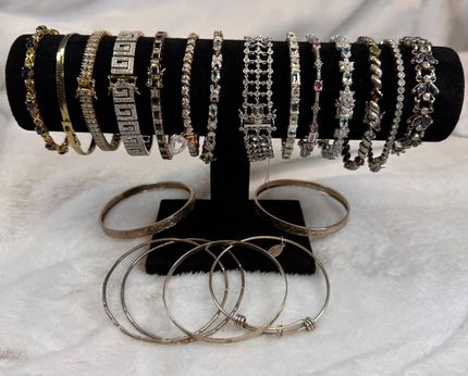 Black jewelry stand displaying stacked gold and silver bracelets and several hoop bracelets below