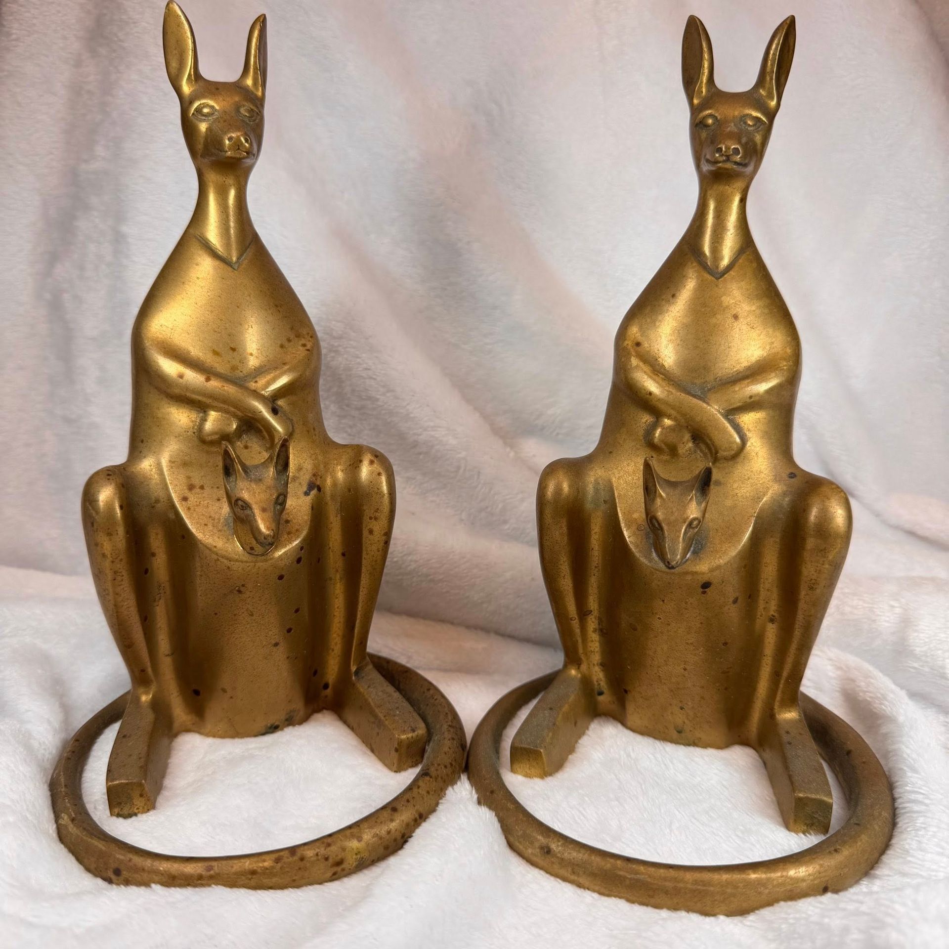 Two gold Egyptian cat statues with crossed front paws on a white cloth background