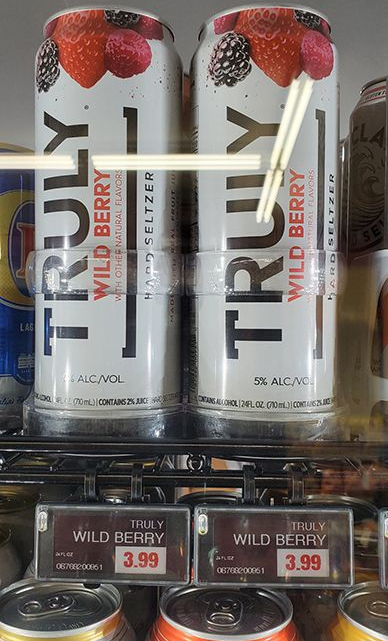 Two cans of Truly Wild Berry hard seltzer on a store shelf with price tags below.