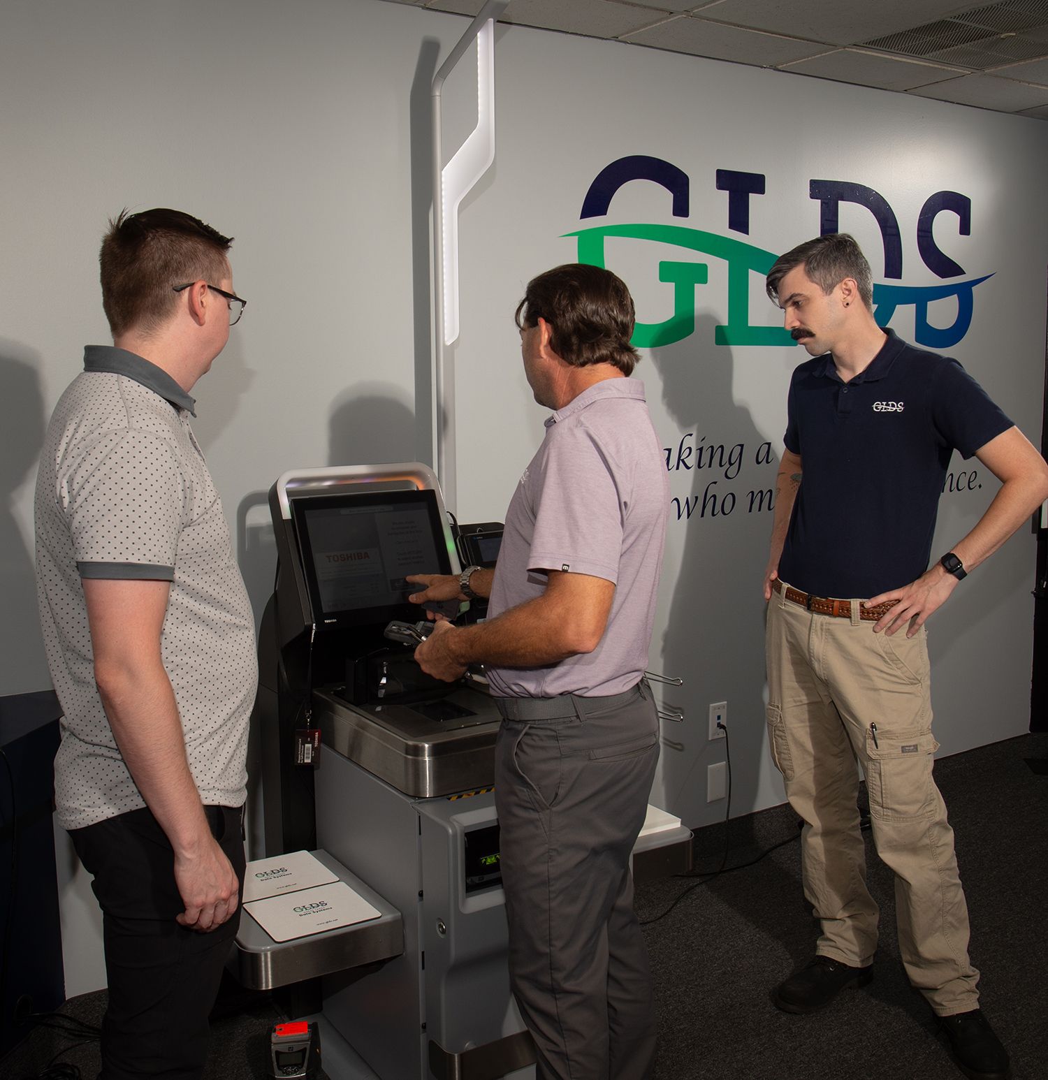 Three men inspecting a machine in an office, with a CTDS sign on the wall.