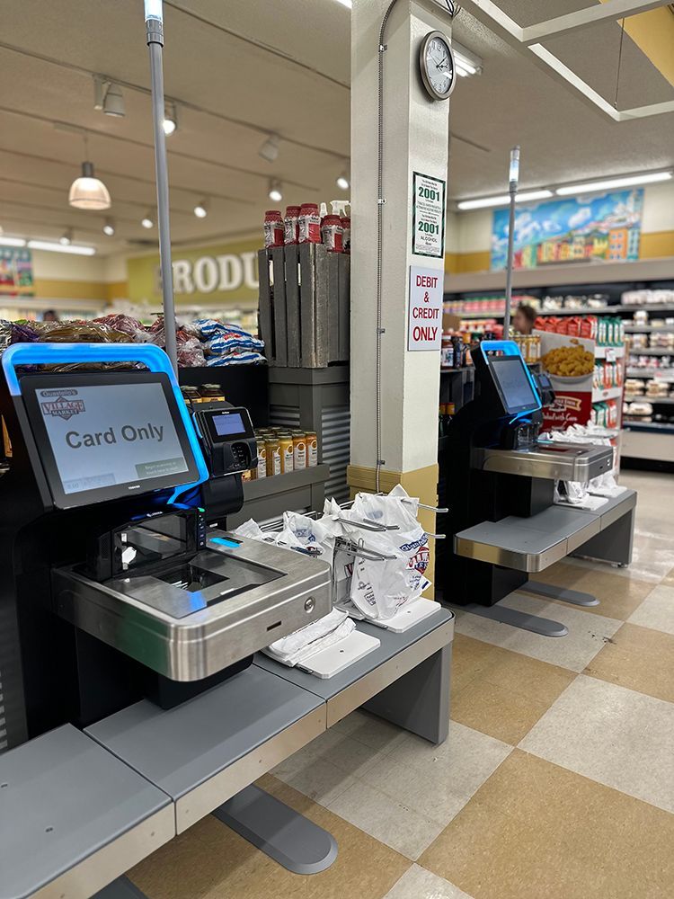 Self-checkout lanes in a grocery store with card-only signs and shoppers using the machines