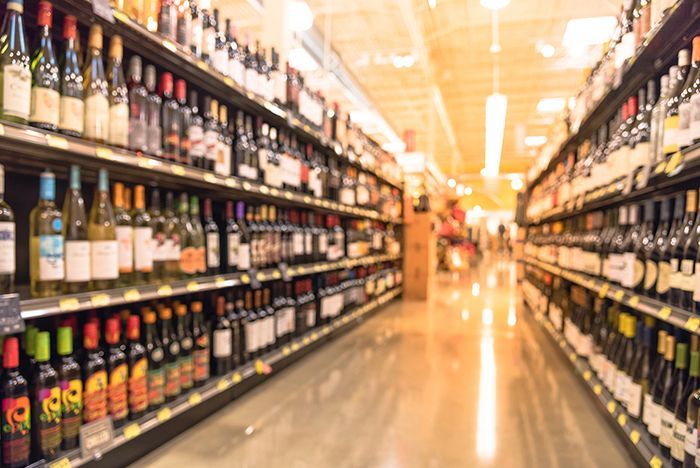 Grocery store aisle lined with wine bottles on shelves, viewed down a bright, polished corridor.