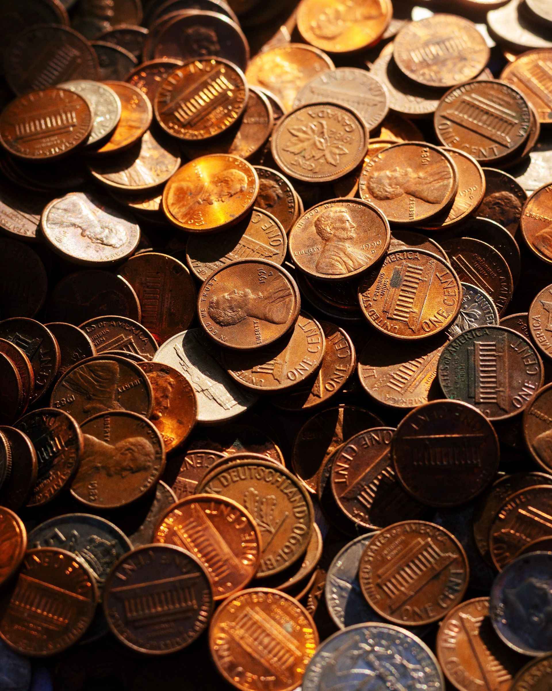 Scattered copper pennies filling the frame, with a few shiny coins catching warm light