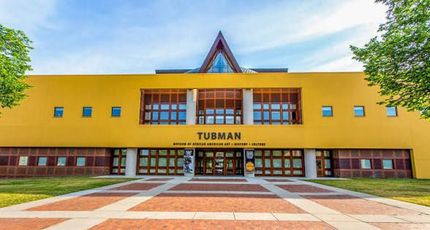 Front view of a yellow TUMAN building with a glass entrance and triangular roof under a blue sky