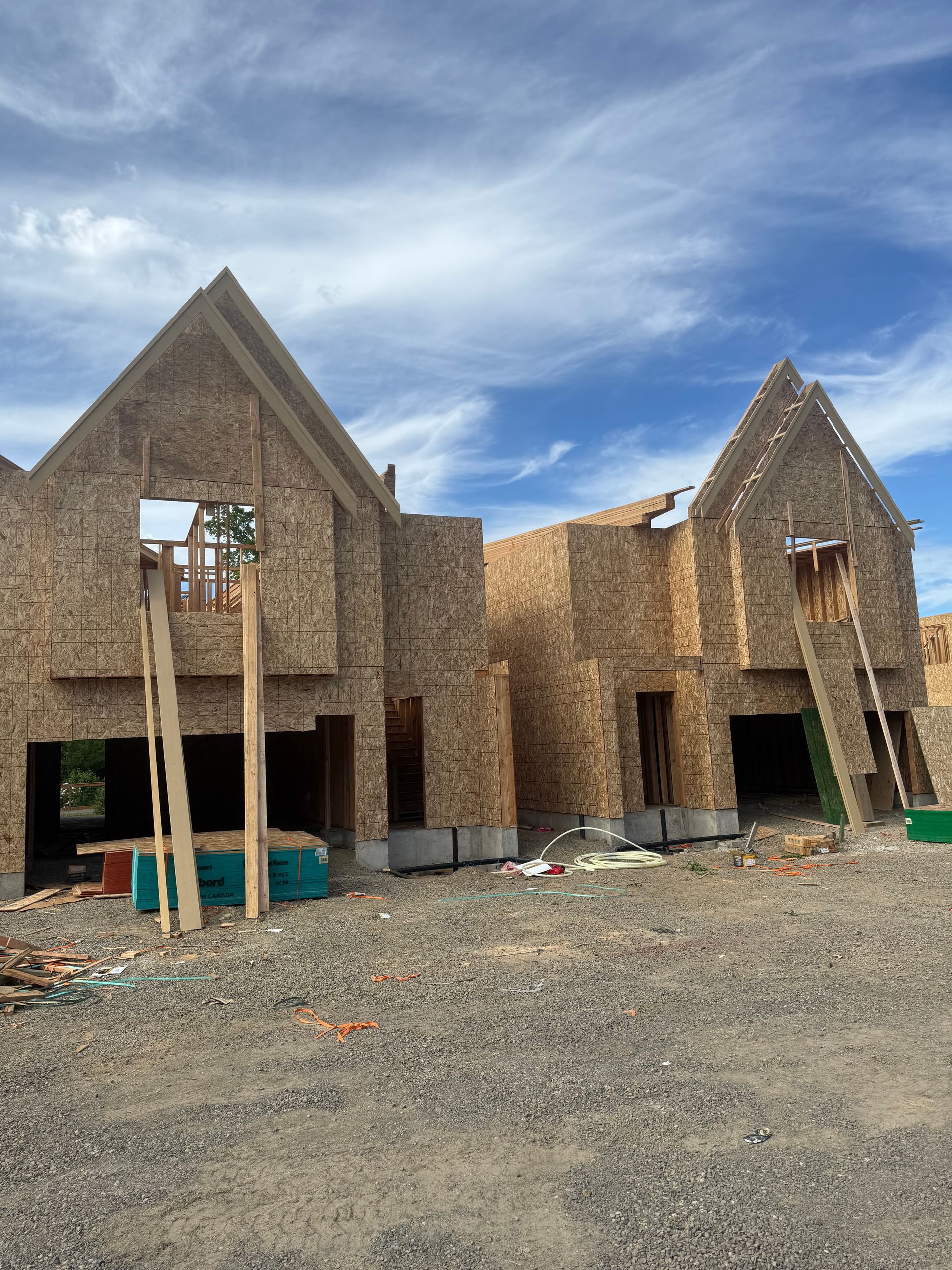 Construction of two connected houses with exposed wood siding and blue sky.