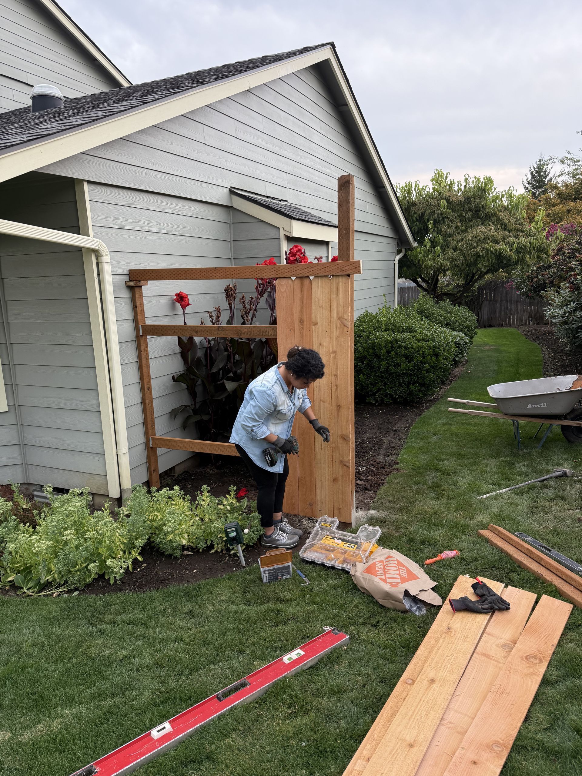 Person building a wooden fence next to a house with a green lawn.