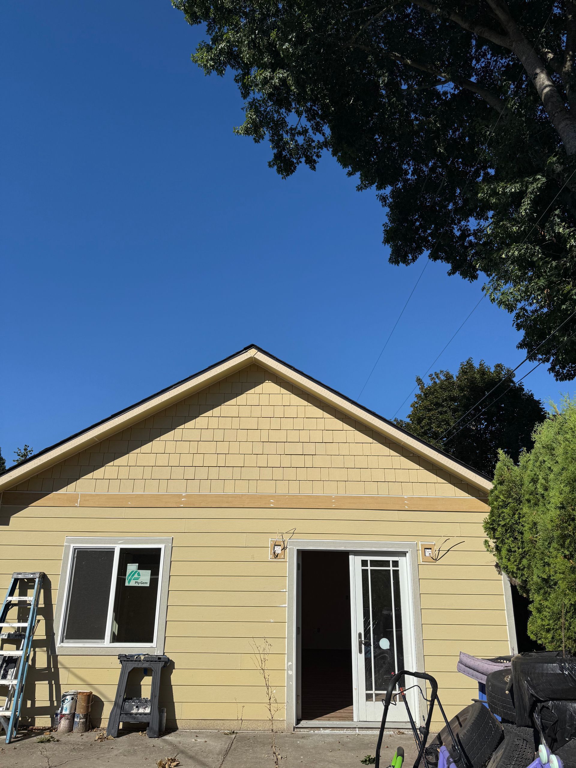 A building under construction with a yellow siding, a new window, and a sliding glass door against a blue sky.