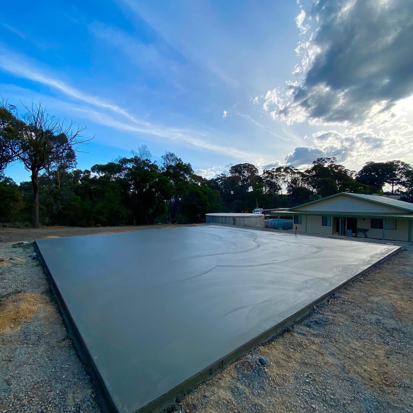Large smooth gray concrete slab beside a house at dusk, with trees and a cloudy sky in the background