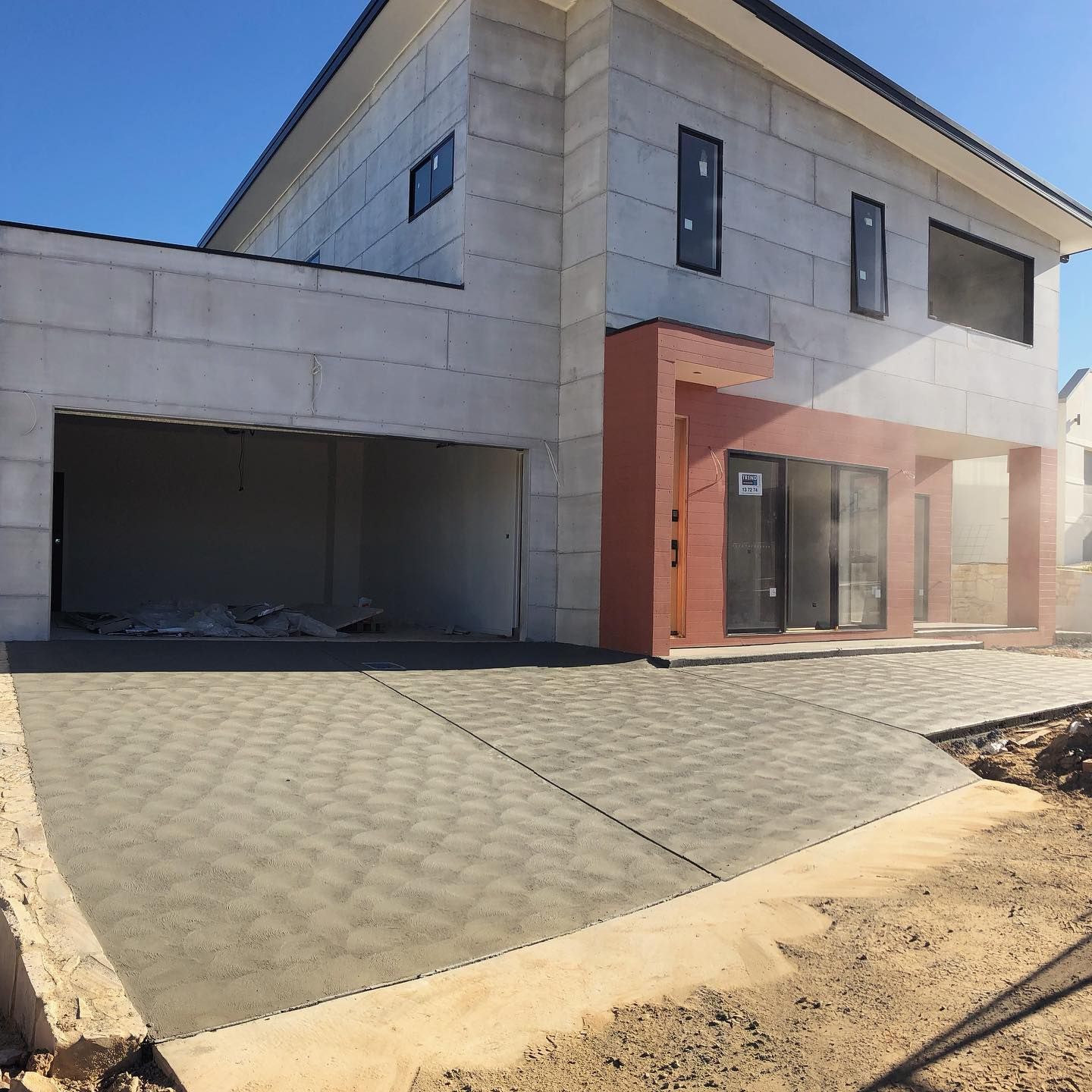 Modern two-story house with unfinished gray walls, red brick accents, and a sloped paved driveway