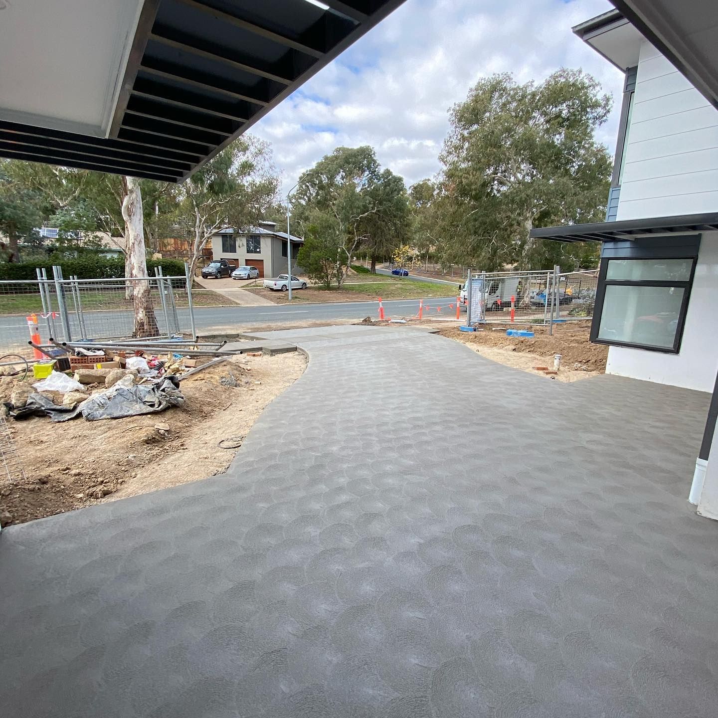 New gray paver driveway at a house under construction, with trees and building materials nearby