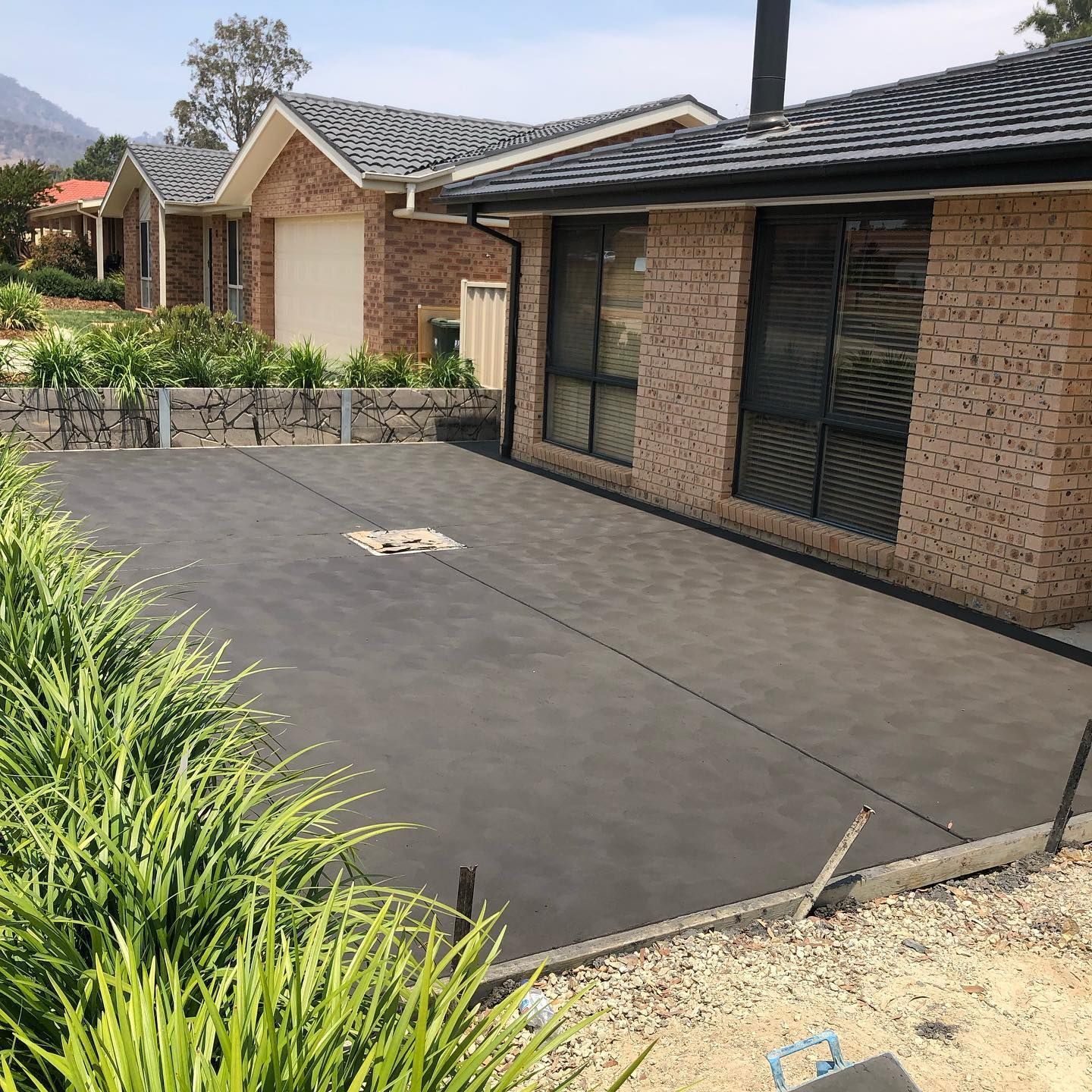 Brick house with a dark paved driveway, garden beds, and a garage in front.