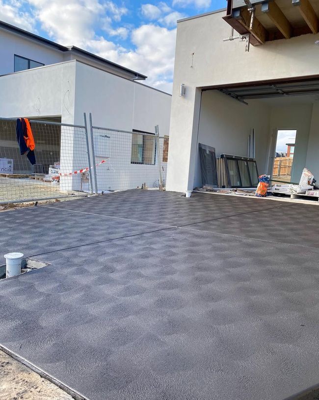 Construction site with a paved driveway, unfinished buildings, and materials near an open garage.