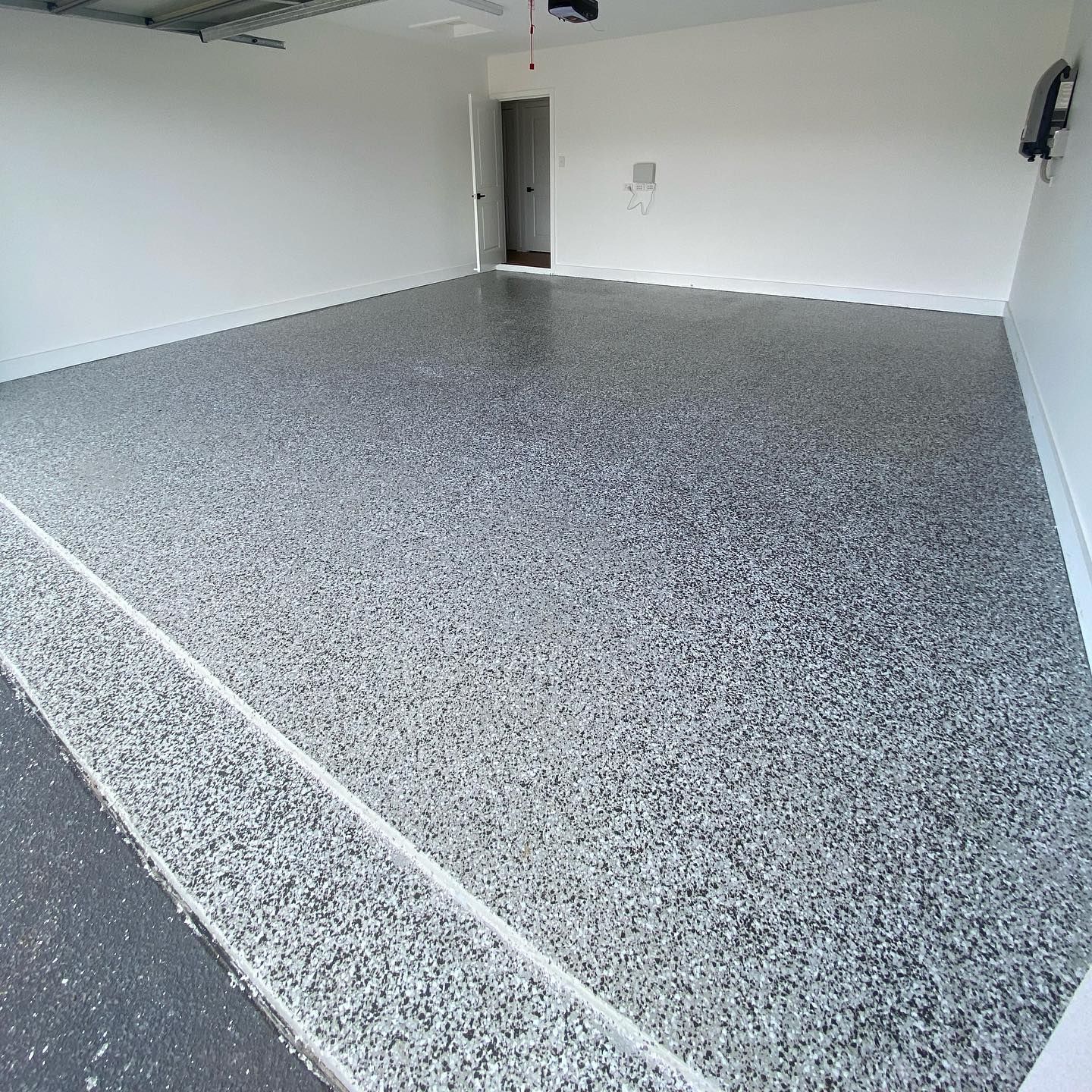 Empty gray epoxy-floored garage with white walls and an open doorway