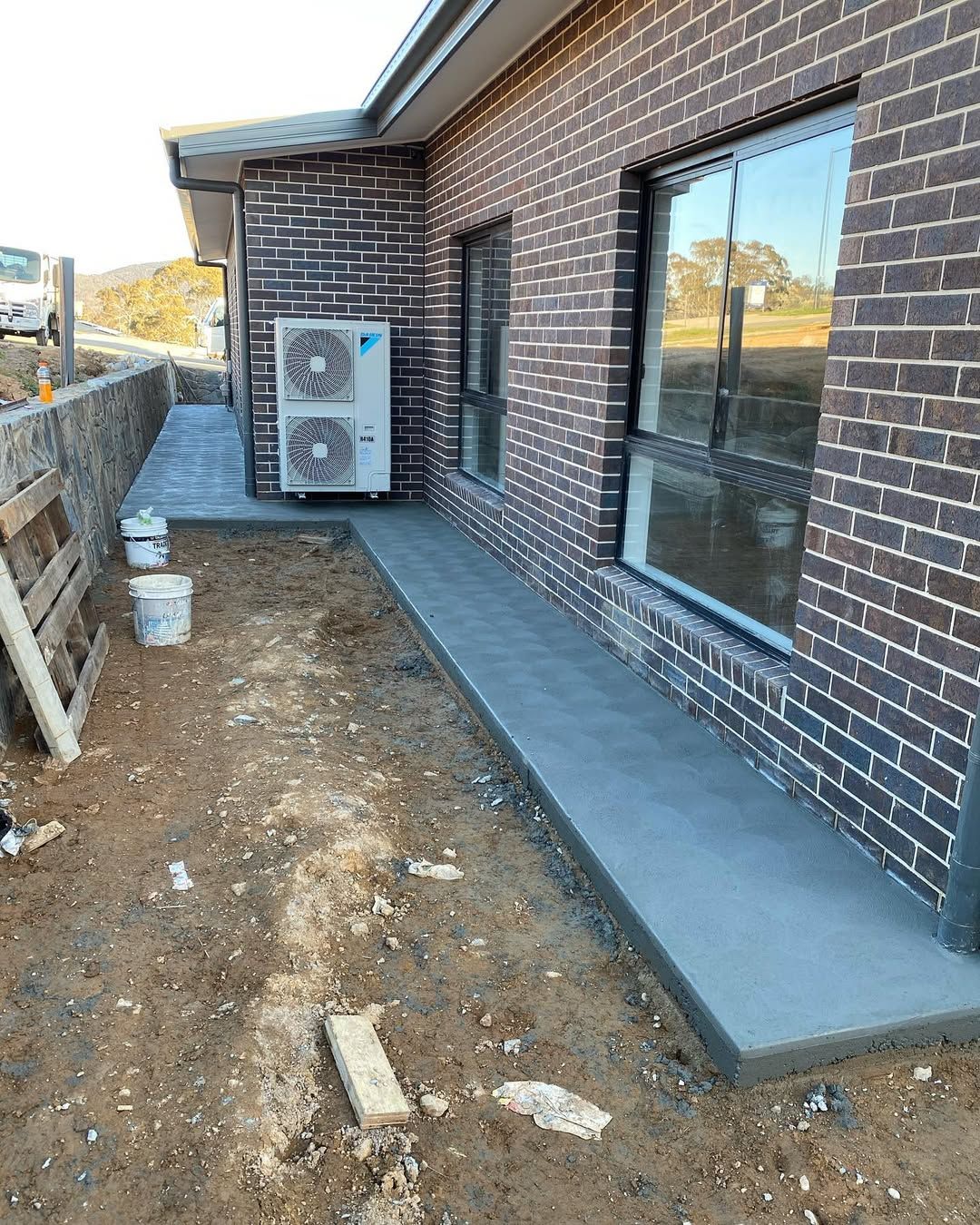Brick house side yard with a concrete walkway, exposed dirt, and an outdoor AC unit.