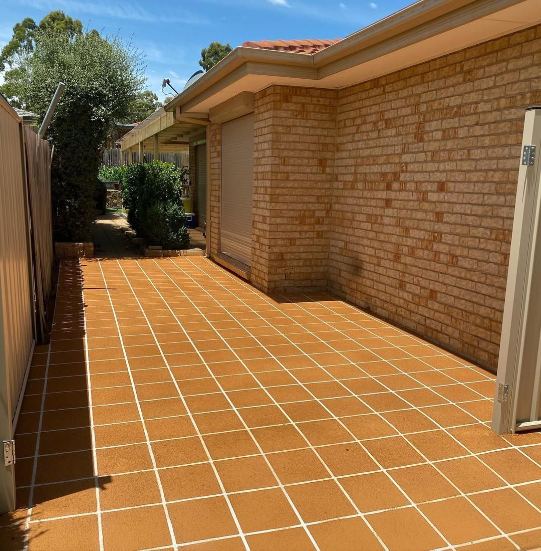 Sunlit brick house side yard with terracotta tile paving and a fence-lined walkway