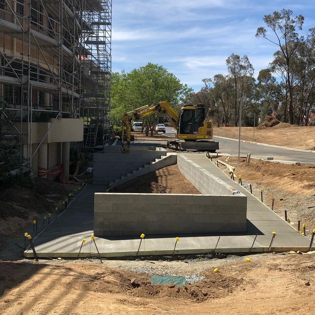 Construction site with scaffolding, excavator, and concrete foundation trench under clear blue sky