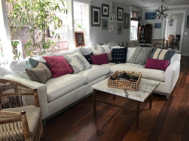 White sectional sofa with colorful pillows in a living room with wood floors and a marble coffee table.