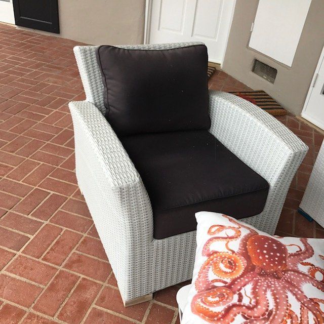 White wicker armchair with brown cushions on a brick patio. Octopus pillow rests in front.