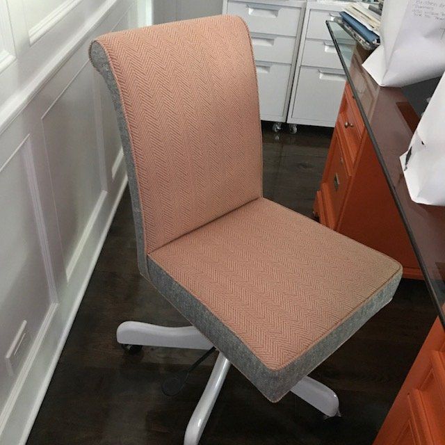 Pink and gray office chair on wheels, in a room with white paneling and an orange desk.