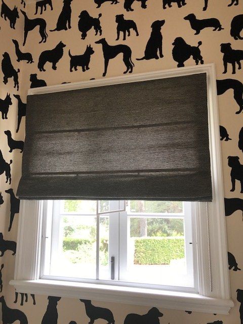 Window with a gray shade, set against wallpaper with black dog silhouettes on a cream background.