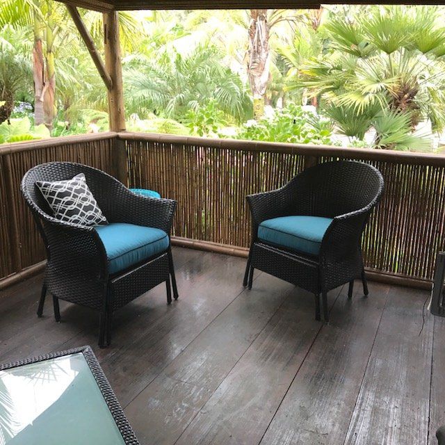 Two wicker chairs with blue cushions on a wooden porch, overlooking lush greenery.