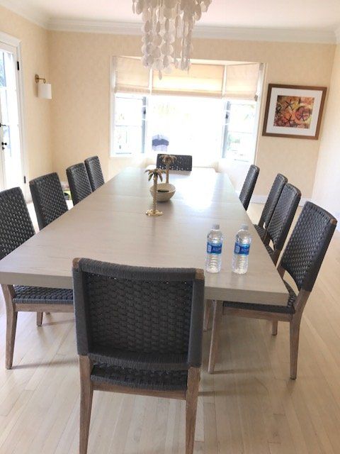 Long dining table set for 12, wicker chairs. Bright room, window, artwork, chandelier.