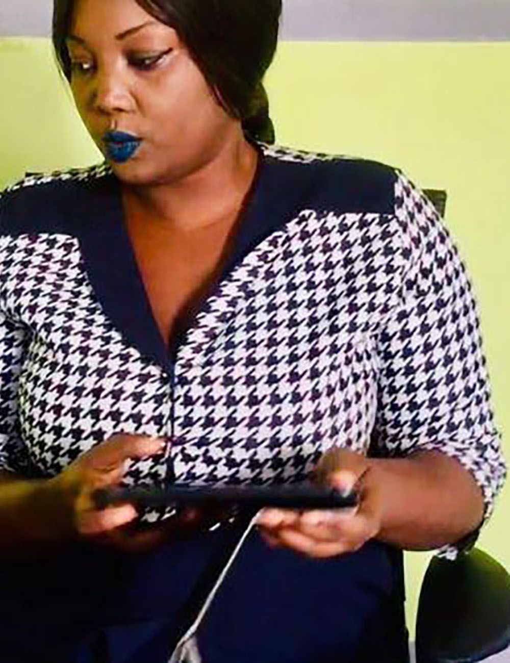 Femme regardant son téléphone portable, vêtue d'une chemise pied-de-poule à bordures bleu foncé.