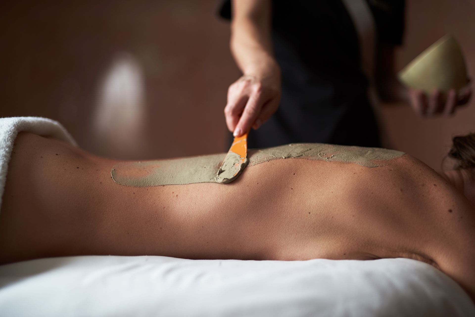 Person applying spa body scrub with a brush to a back on a massage table