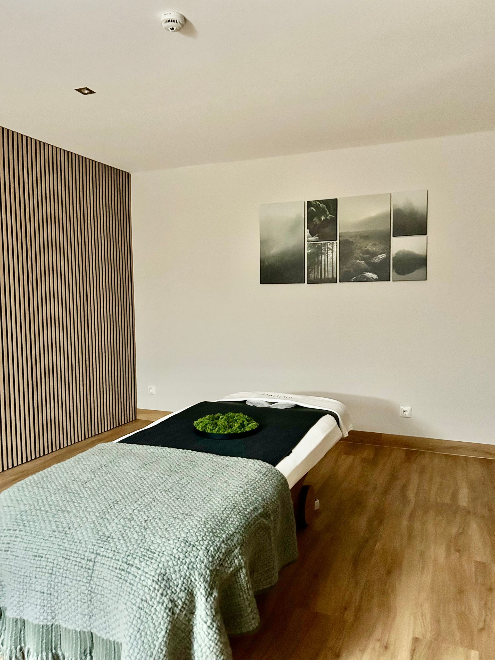 Minimal bedroom with a bed, black-and-green bedding, patterned accent wall, and framed wall art
