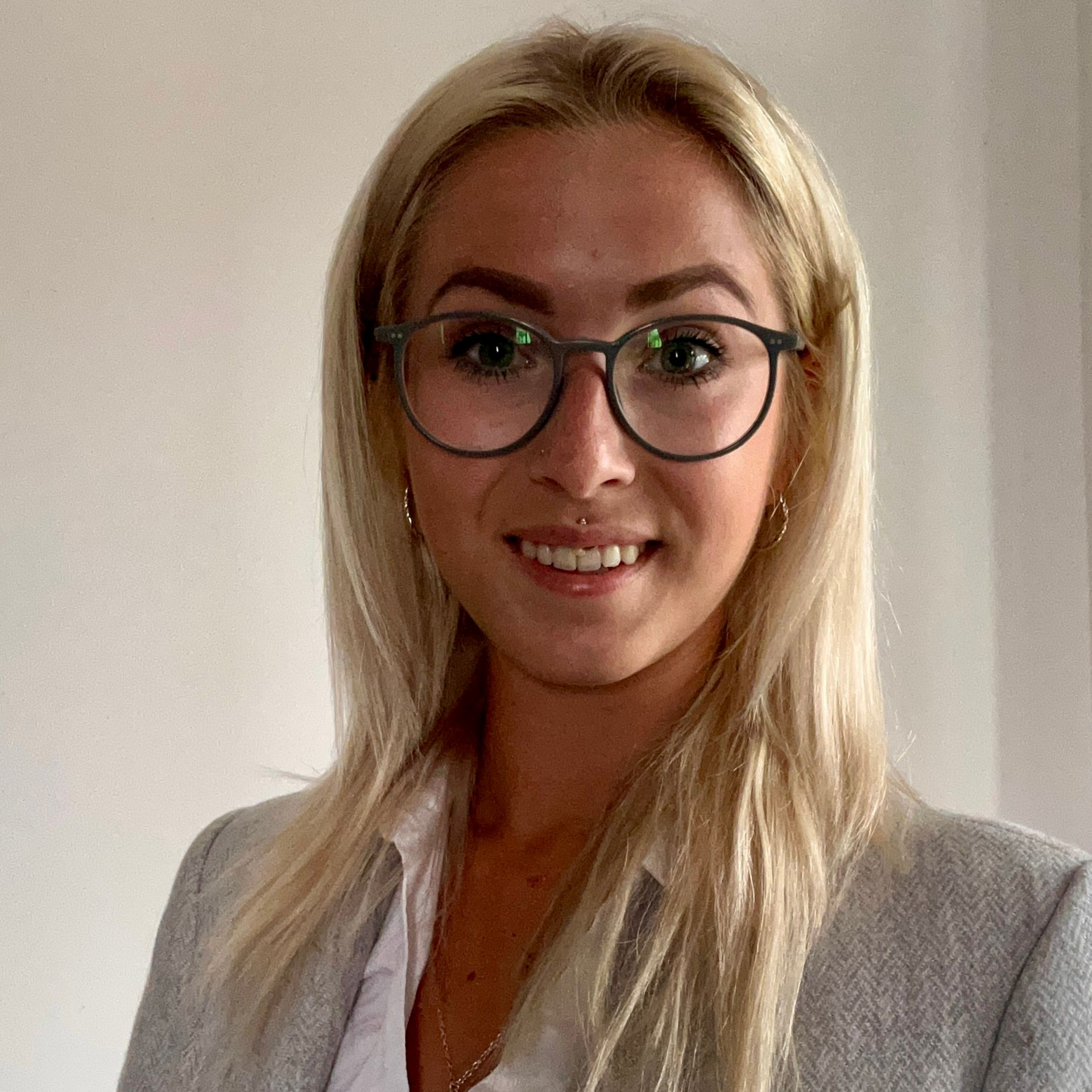 Portrait of a smiling woman with blonde hair and glasses in a gray blazer indoors