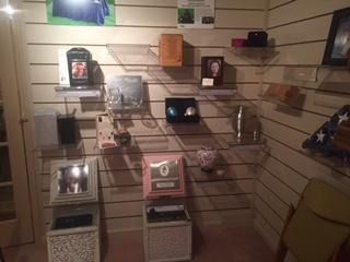 Shelves on a paneled wall displaying various memorial urns, small keepsakes, and a folded American flag.