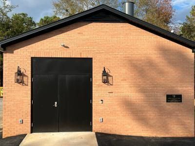 A tan brick building exterior with black double doors, black trim, and two wall-mounted lanterns.