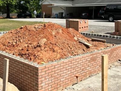 A rectangular brick wall foundation filled with a mound of dirt at an outdoor construction site.