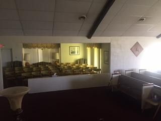 A room with rows of pews facing a large mirror that reflects a similar seating area, creating an illusion of more space.