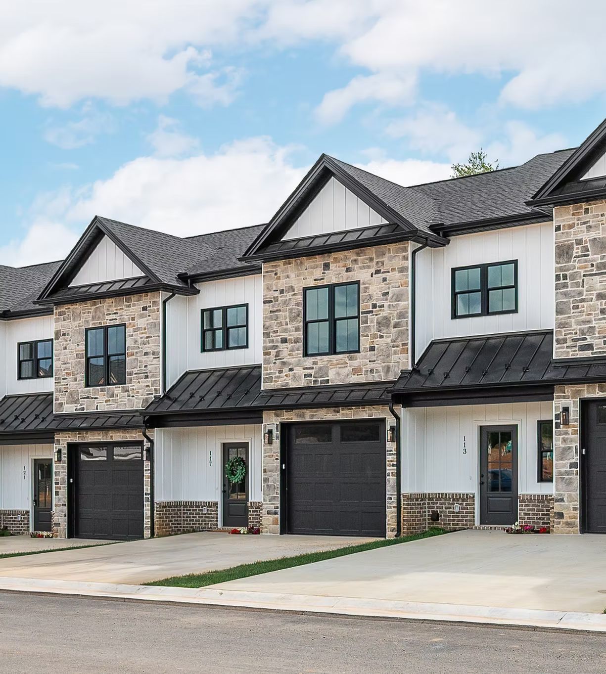 Row of modern stone townhouses with black roofs and garages along a quiet street