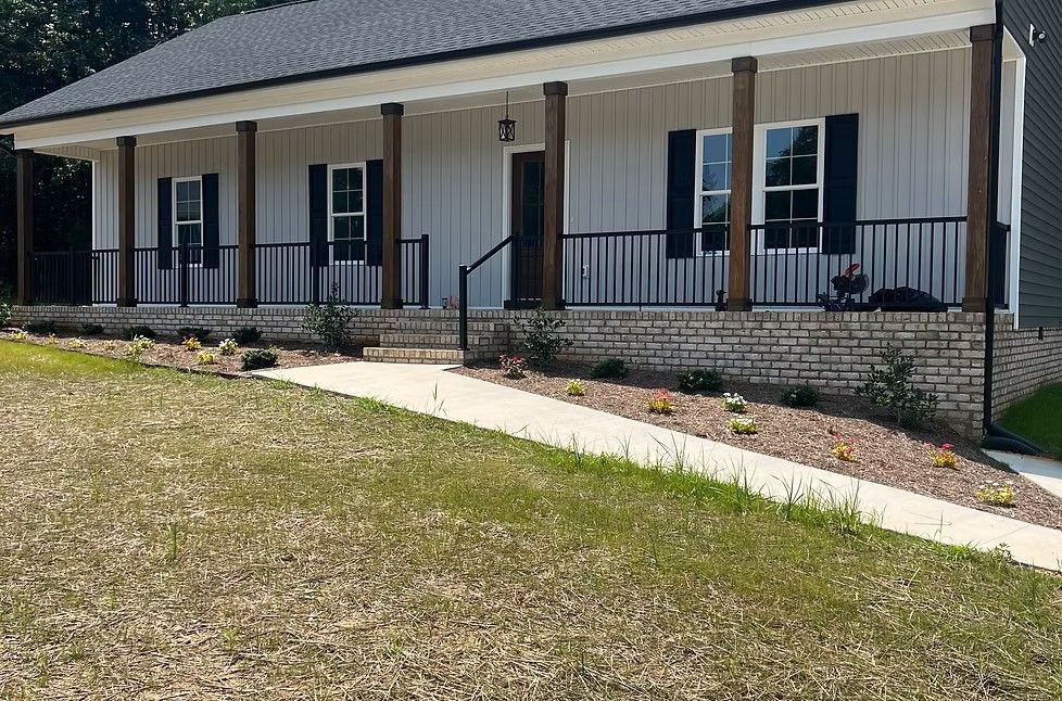 Single-story house with a front porch, black shutters, and a sloped lawn and walkway.