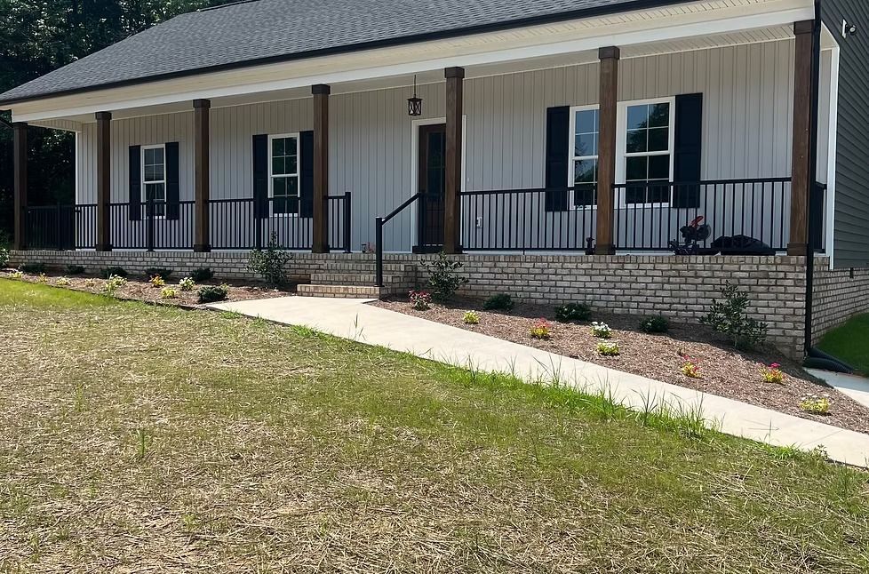 Single-story house with a front porch, black shutters, and a sloped sidewalk across a lawn.