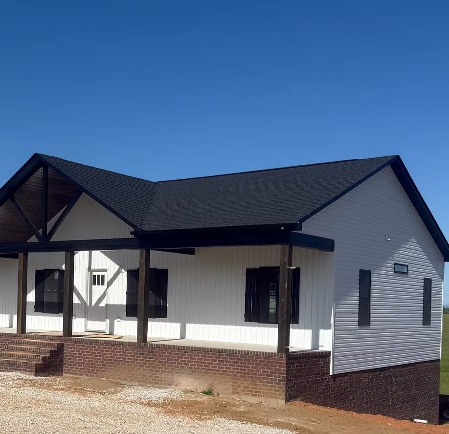 Single-story white house with black roof and porch under a clear blue sky