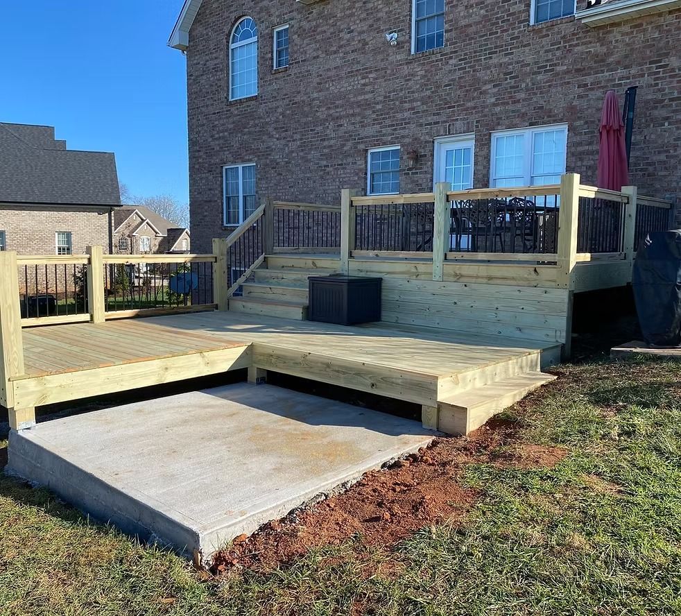 Backyard deck with wooden steps and concrete patio beside a brick house