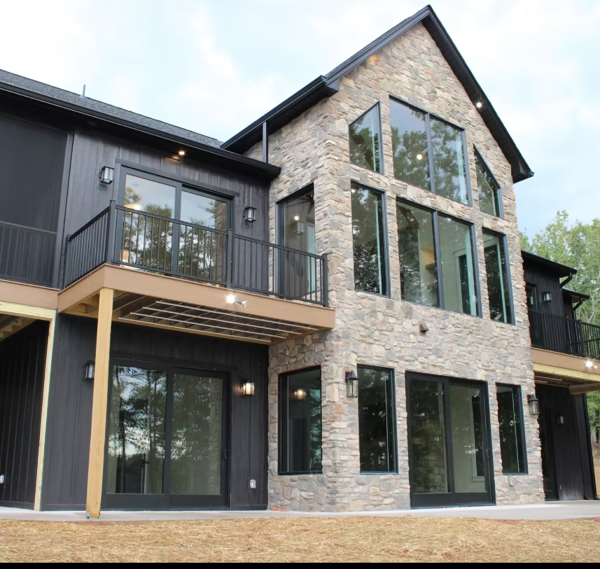 Modern two-story house with stone facade, black siding, large windows, and a small balcony