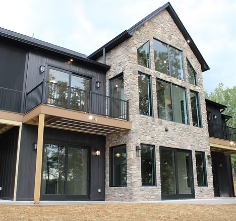 Modern two-story house with black siding, stone facade, and large windows and balcony