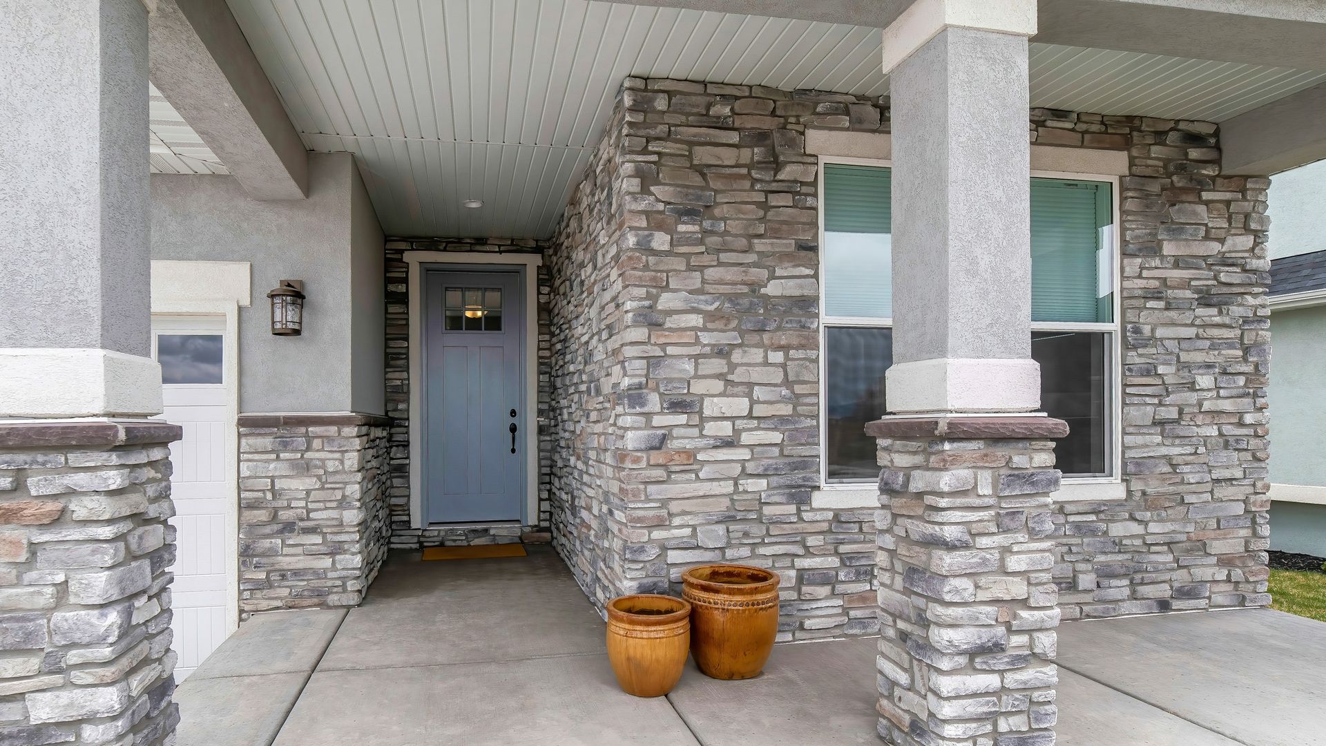 Front porch with stone columns, a gray front door, and two brown pots on the concrete entryway.