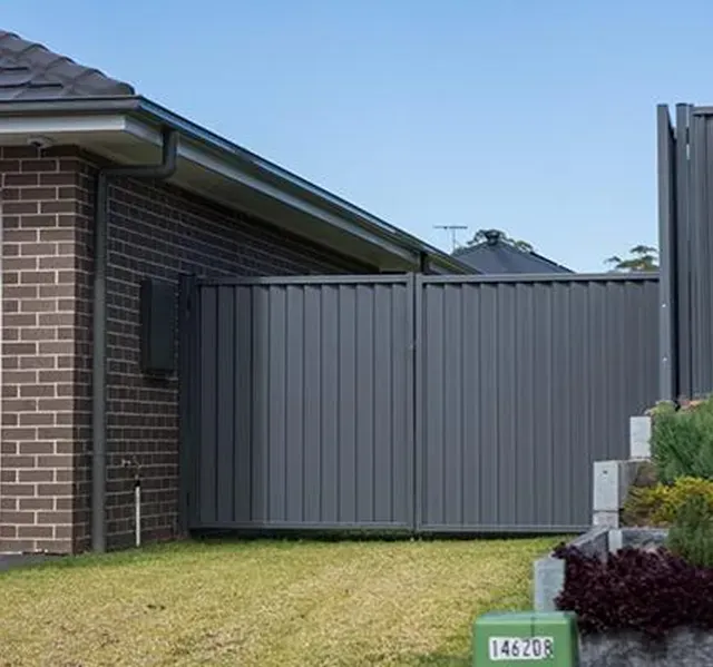Grey metal gate next to a brick house with a green lawn and bushes.
