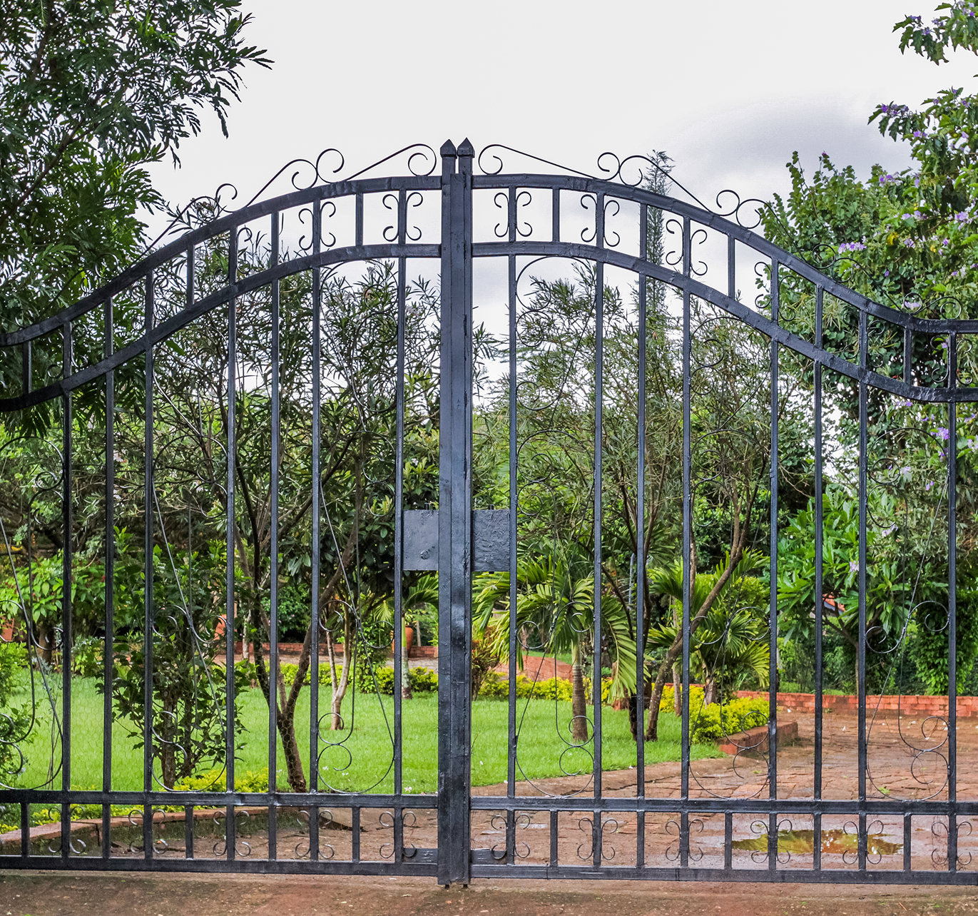 A wrought iron gate is open to a lush green field surrounded by trees.
