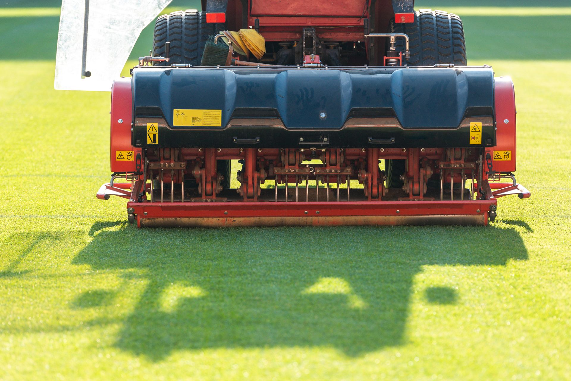 Rear view of a red lawn mower trimming bright green grass in sunlight