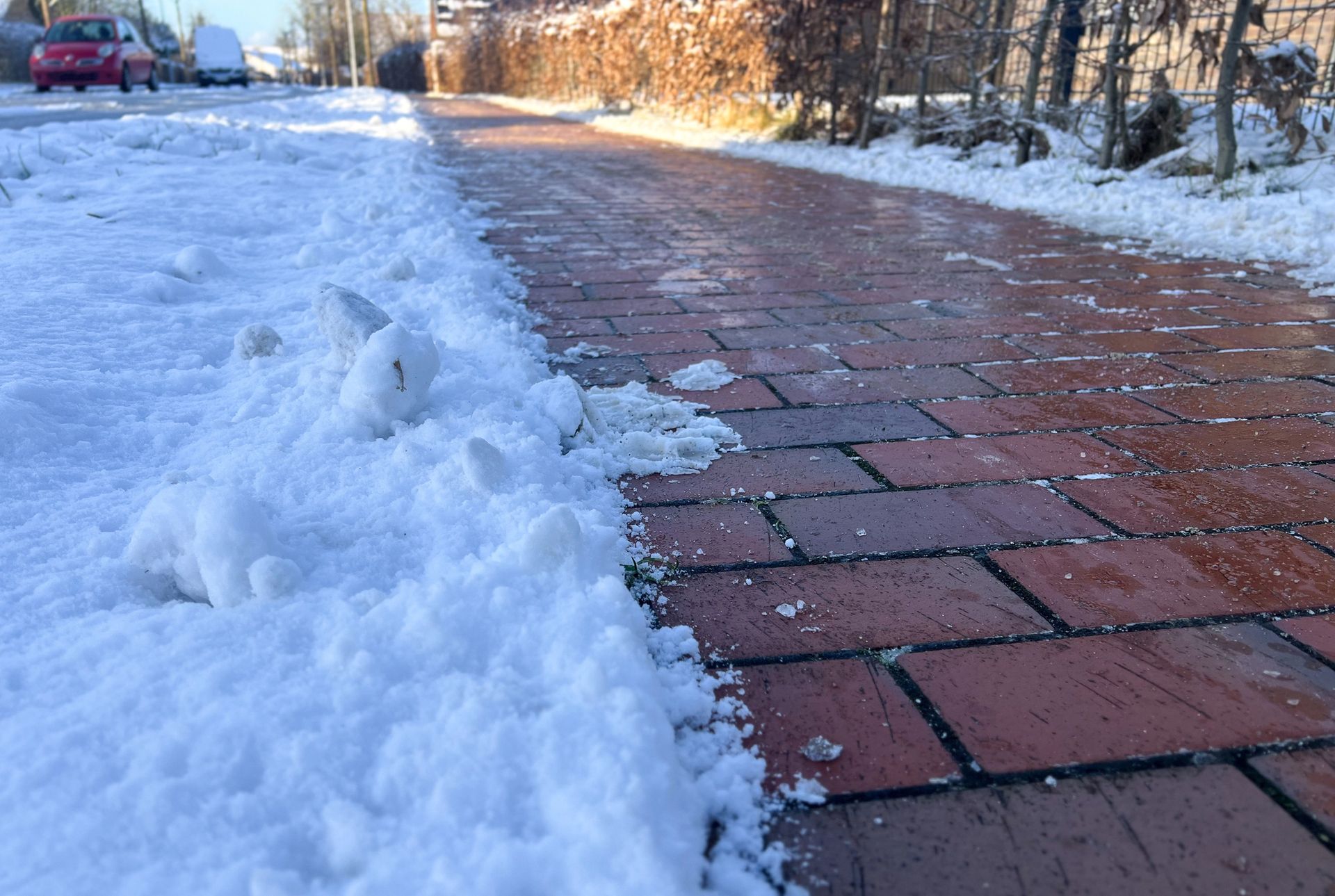 Snow-covered brick path with a cleared walkway and parked car in the background